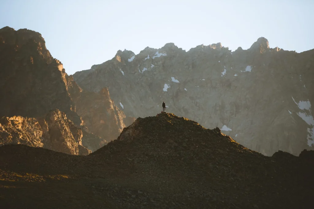 person standing at top of mountain peak overlooking rocky mountain range